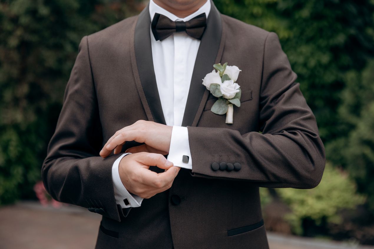 Bräutigam in elegantem Hochzeitsanzug mit weißer Rose und Manschettenknopf, passende Accessoires zu Eheringe Platin
