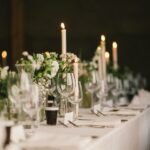 Stilvoll gedeckter Hochzeitstisch mit Kerzen, weißen Blumen und Glasglaesern – stimmungsvolle Kulisse für Eheringe Platin