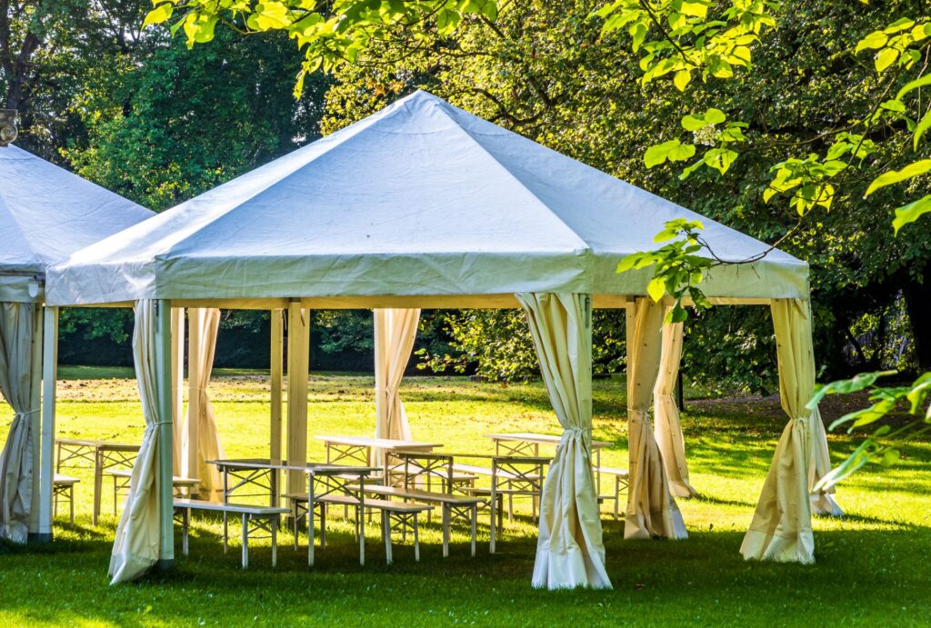 Offener gartenpavillon mit weissen vorhaengen und sitzgelegenheiten im sommer, dekorativ und wetterfest