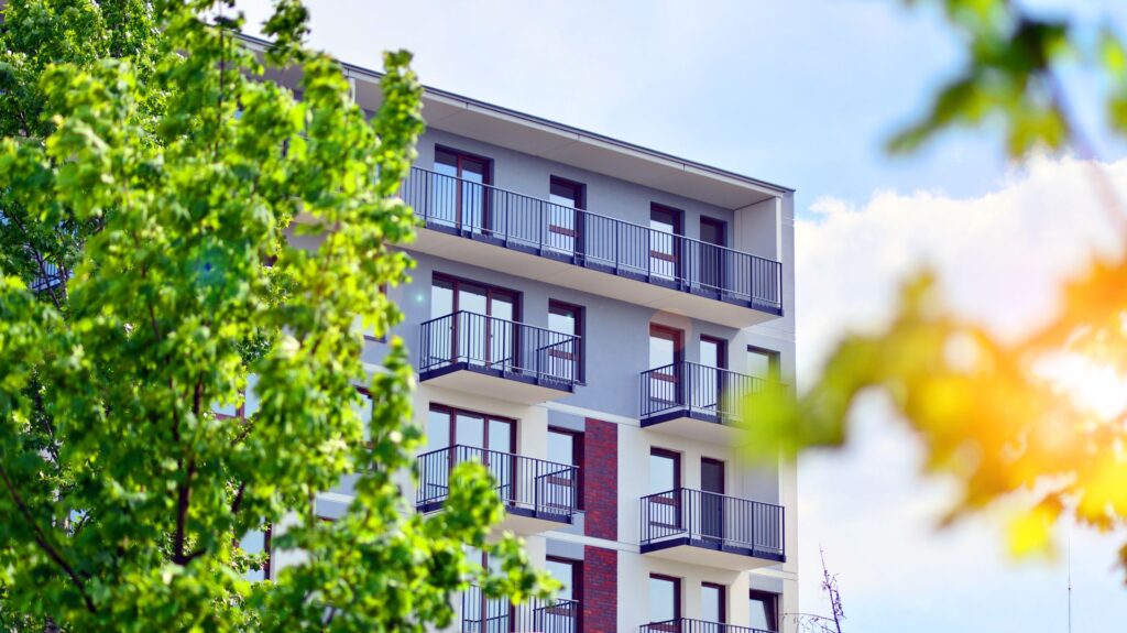 Mehrgeschossiges Wohnhaus mit Balkonen und Gruenflaeche – typisches Umfeld fuer Schallschutzzaeune auf Baustellen in Wohngebieten