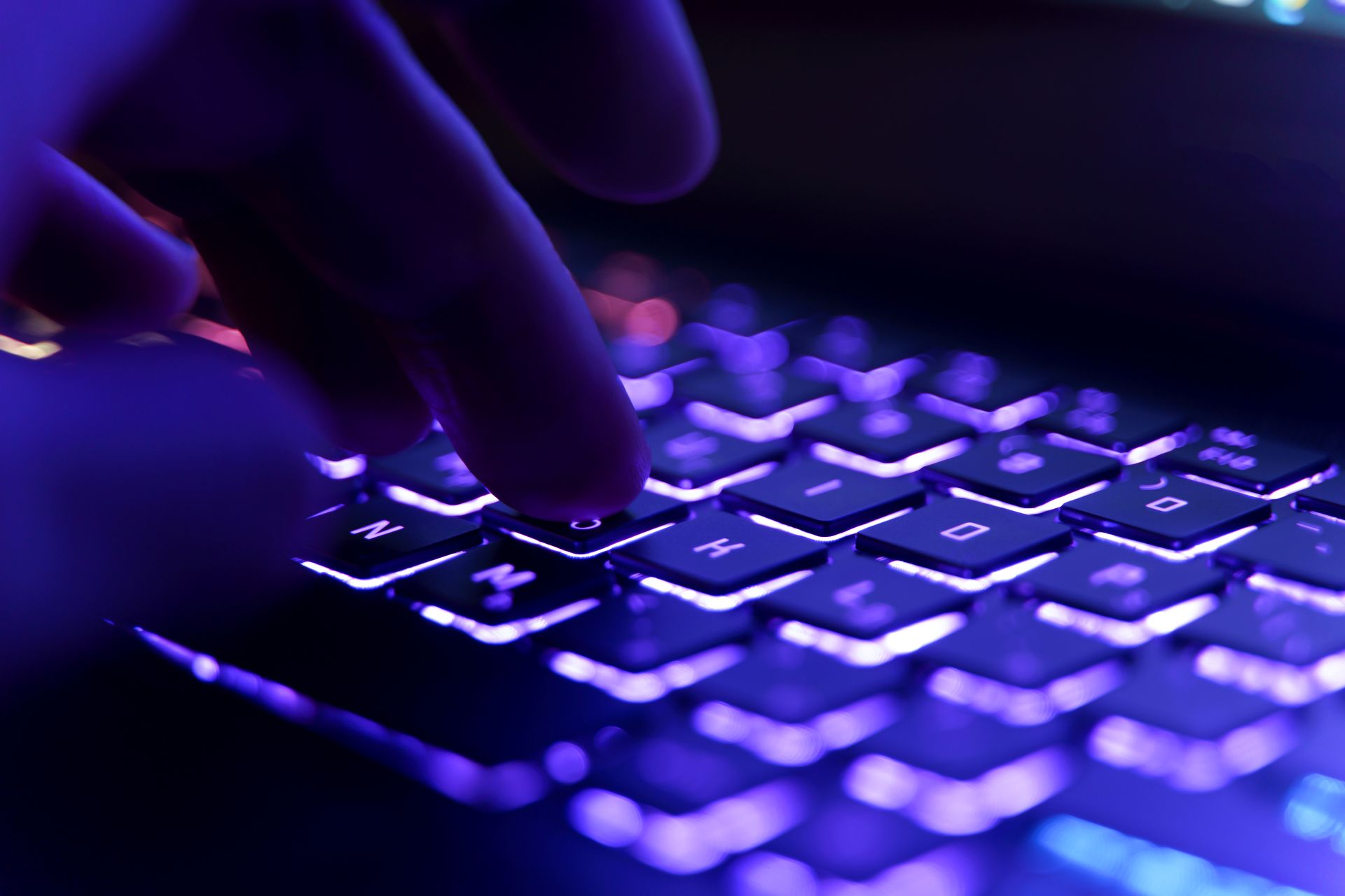 Hand tippt auf leuchtender RGB-Tastatur in dunkler Gaming-Umgebung.