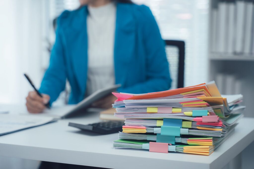 Ordner und Papierstapel auf Schreibtisch im Buero, Symbol fuer hohen Verwaltungsaufwand und Bedarf an professioneller Lohnabrechnung durch ein Lohnbuero