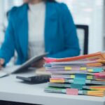 Ordner und Papierstapel auf Schreibtisch im Buero, Symbol fuer hohen Verwaltungsaufwand und Bedarf an professioneller Lohnabrechnung durch ein Lohnbuero