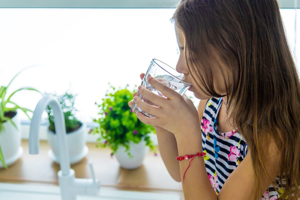 Osmose Wasser Trinken – Kind hält Glas mit klarem Wasser in heller Küche mit Pflanzen